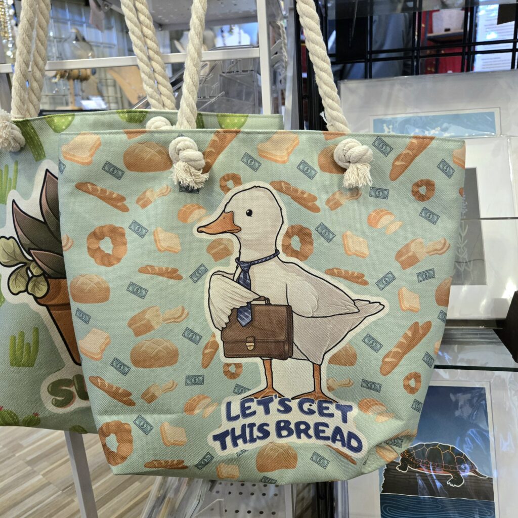 Kawaii animated style tote bag of duck holding brief case, saying let's get this bread